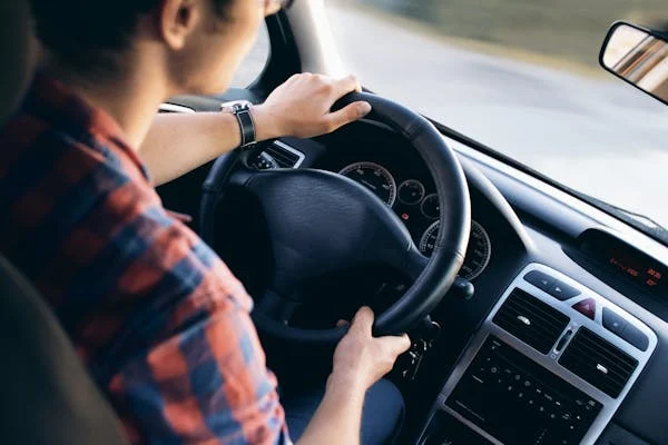 Professional car driver in Dubai wearing a casual plaid shirt, driving a modern vehicle with a firm grip on the steering wheel, ensuring a smooth ride.